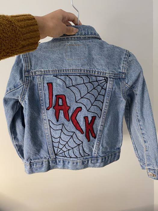 Back of a kids denim jacket embroidered with JACK in red over a spiderweb