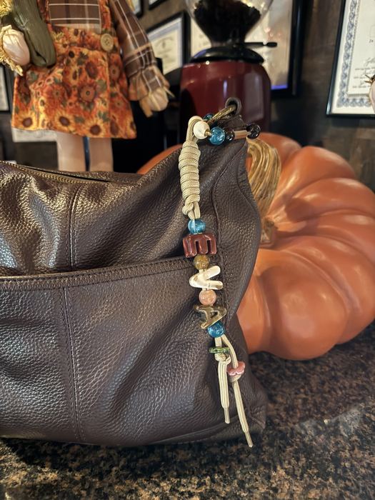 Tan chunky letter bead keychain on a leather bag