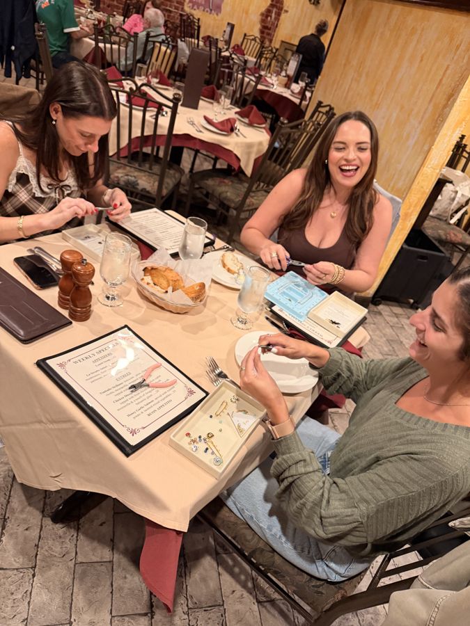 Three women making charm pieces at a restaurant table during a Hoop & Hand pop-up