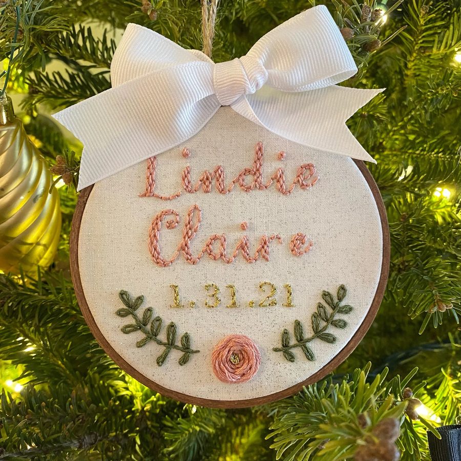 Ornament hand-embroidered with Lindie Claire and 1.31.21 in pink and gold, with a pink rosette and green leaves, on a Christmas tree