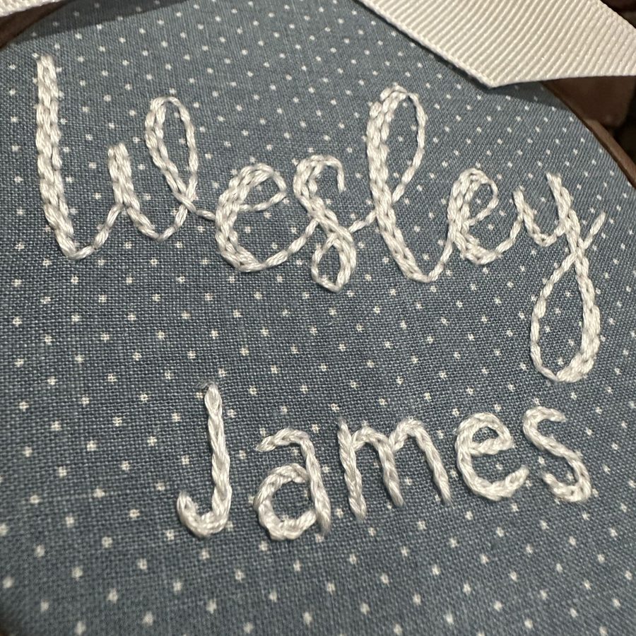 The name Wesley James hand-embroidered in white on blue polka dot fabric
