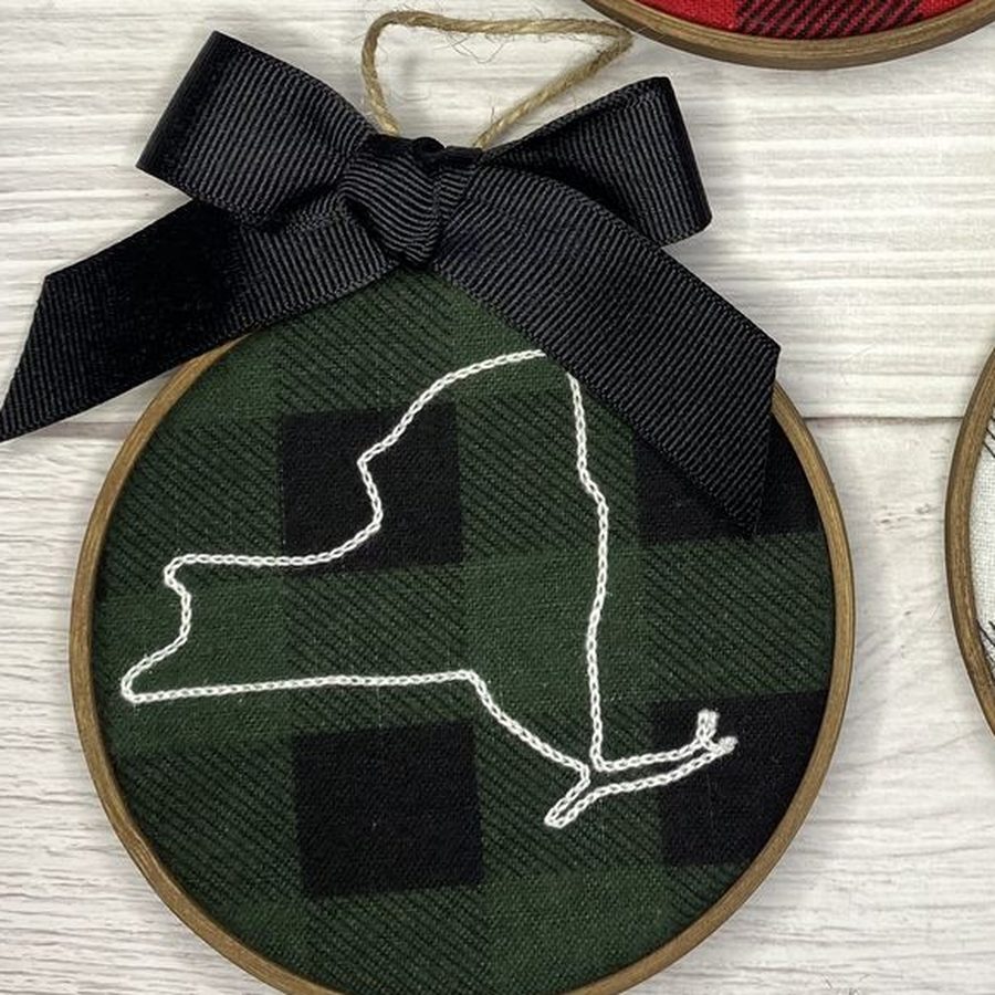 Green buffalo check hoop ornament stitched with a white outline of New York and a black bow
